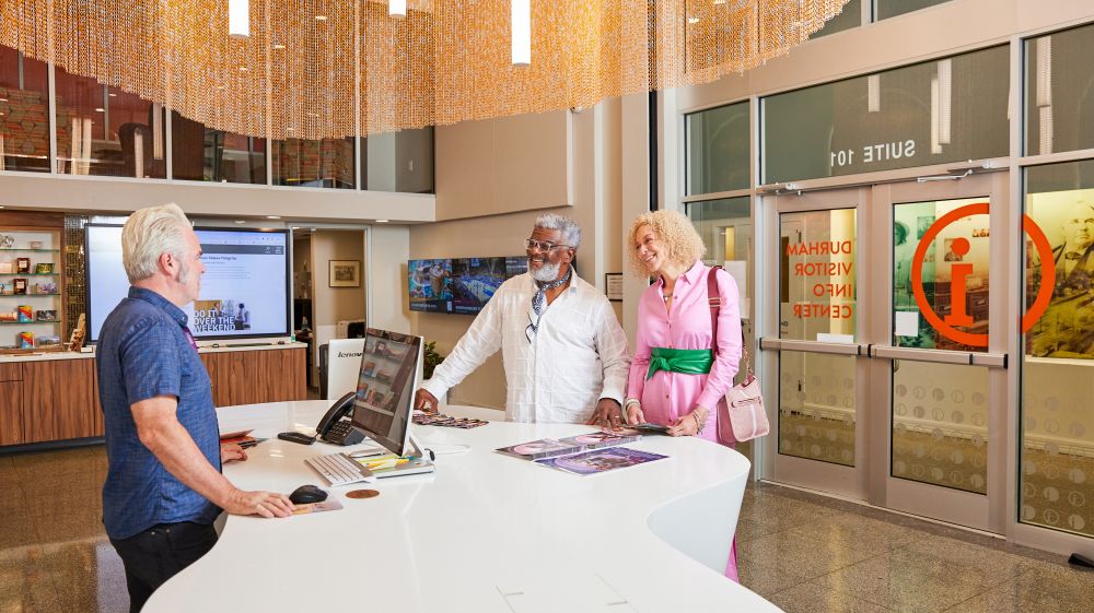 A couple speaks with someone behind a desk at the Visitor Info Center in Durham, NC.