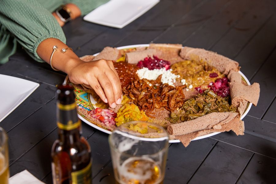 a hand dips bread into a colorful combination platter from Goorsha.