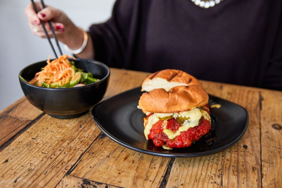 A customer digs into a bowl with chopsticks as a chicken sandwich waits patiently nearby to be enjoyed.