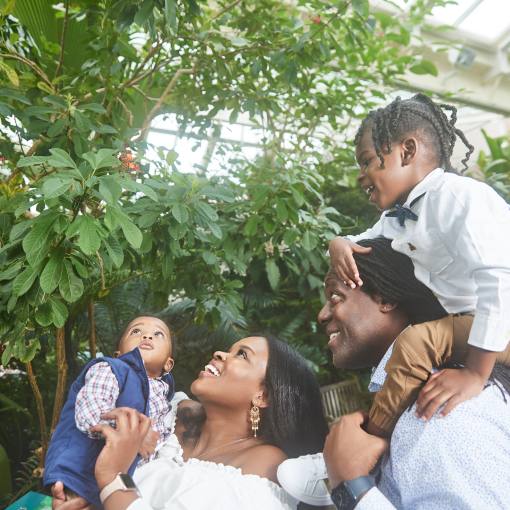 A family gazes upon a butterfly in front of lush green foliage at the Museum of Life and Science.