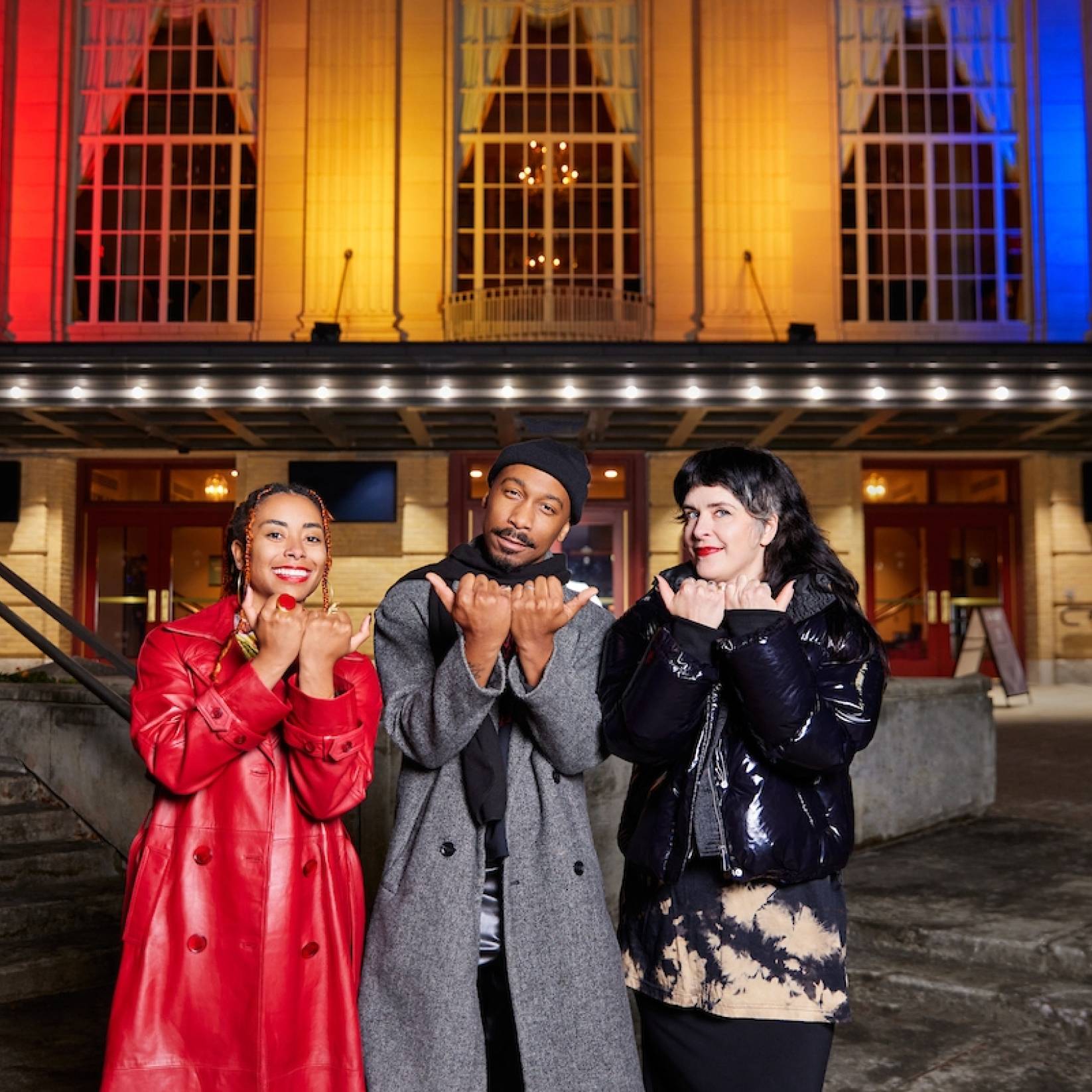 People pose outside The Carolina Theatre, featuring a light display showcasing the city of Durham's flag colors on the facade