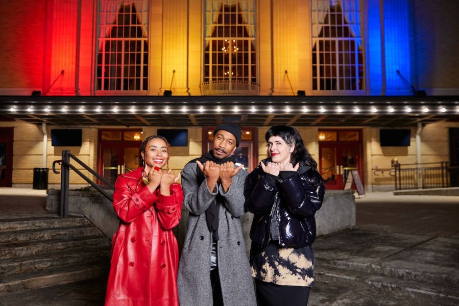 People pose outside The Carolina Theatre, featuring a light display showcasing the city of Durham's flag colors on the facade