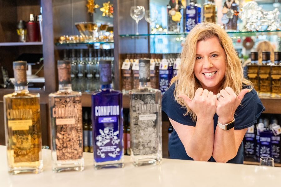 Melissa Katrincic makes bull horns and poses with her award-winning Conniption Gin behind the bar at Durham Distillery.