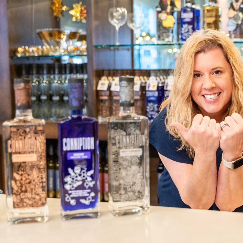 Melissa Katrincic makes bull horns and poses with her award-winning Conniption Gin behind the bar at Durham Distillery.