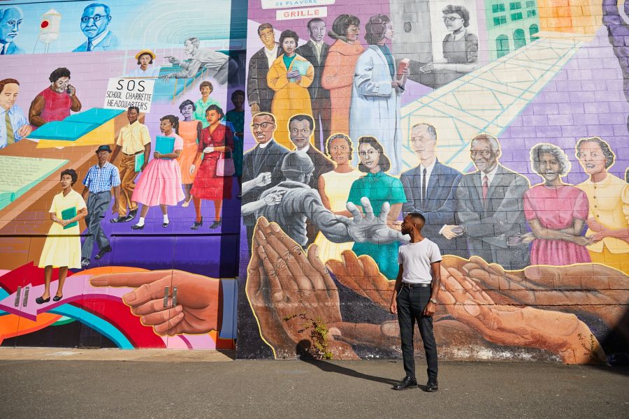 A man stands in front of one of Durham's Black history murals.