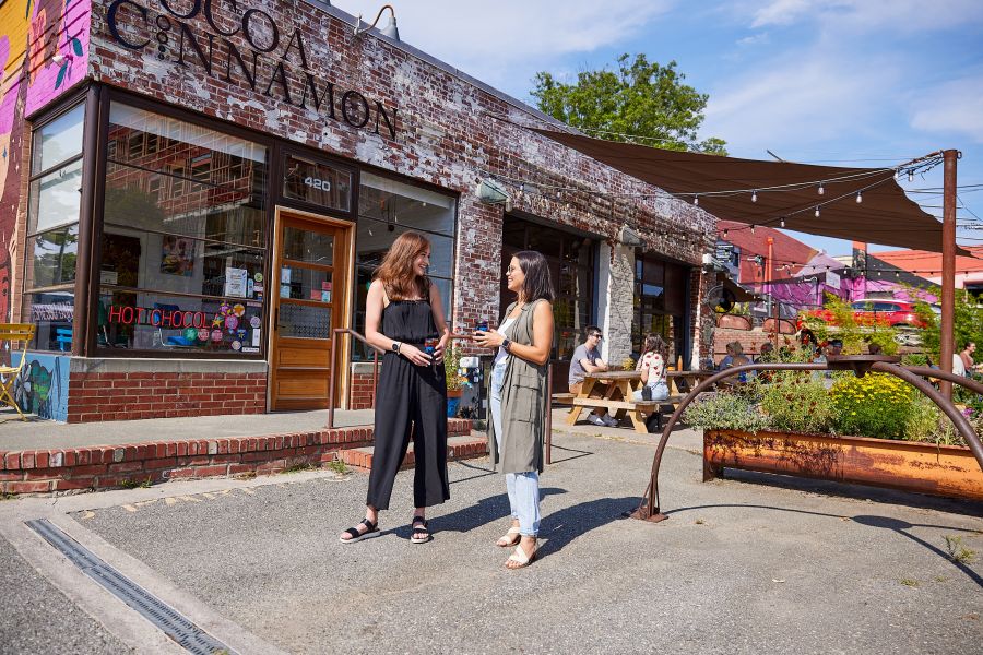 Two woman stand talking in front of Cocoa Cinnamon on a sunny day in Durham.