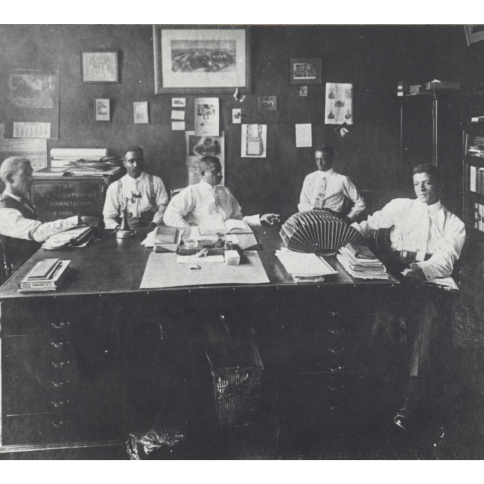 A black and white photo shows a group of men sitting around a desk at NC Mutual in Durham, NC.