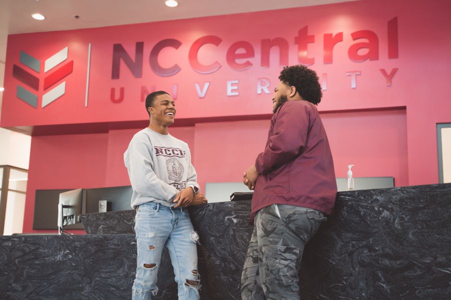 Students talking and laughing in the new student center in front of a NC Central University sign.