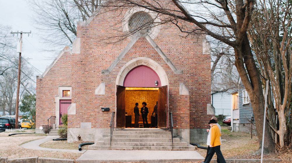 A person walks in front of a Gothic church converted into an arts space. The door is open and people are inside.