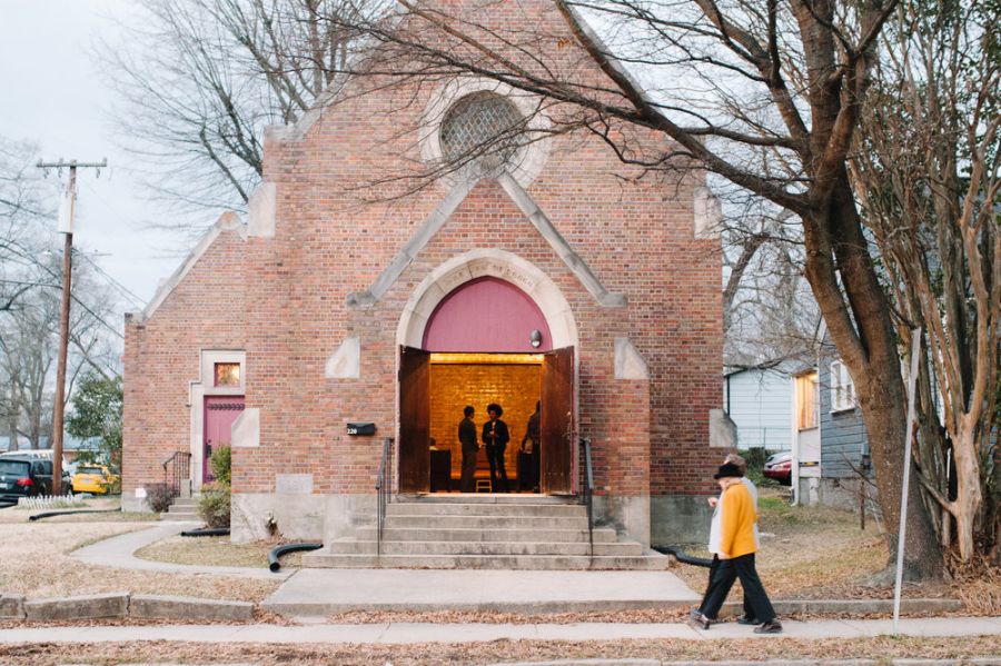A person walks in front of a Gothic church converted into an arts space. The door is open and people are inside.