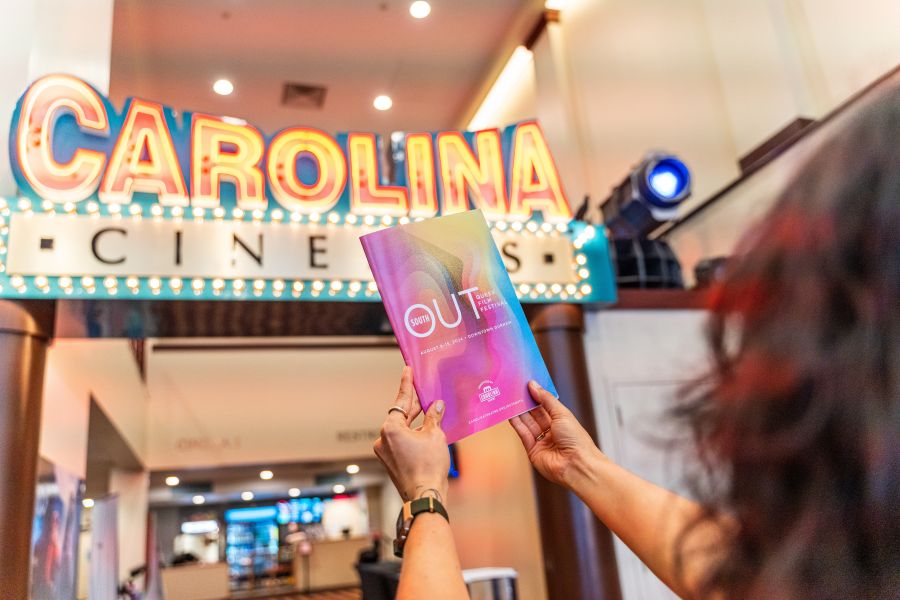 Hands hold up a pamphlet for the OUTSOUTH Queer Film Festival at the Carolina Theatre in Durham.