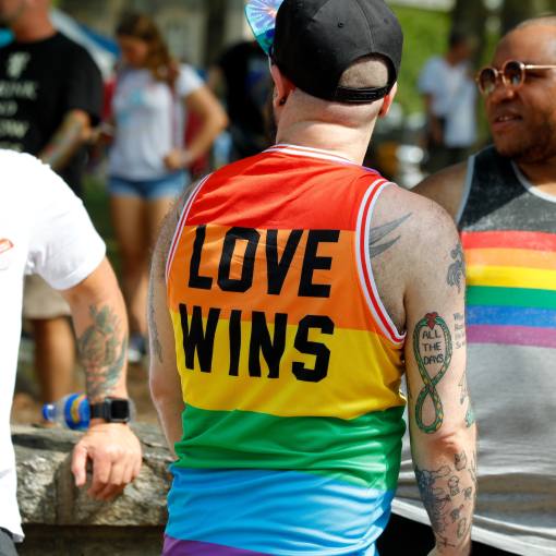 A pride parade goer wearing a &quot;love wins&quot; rainbow tanktop laughs with others at the parade.