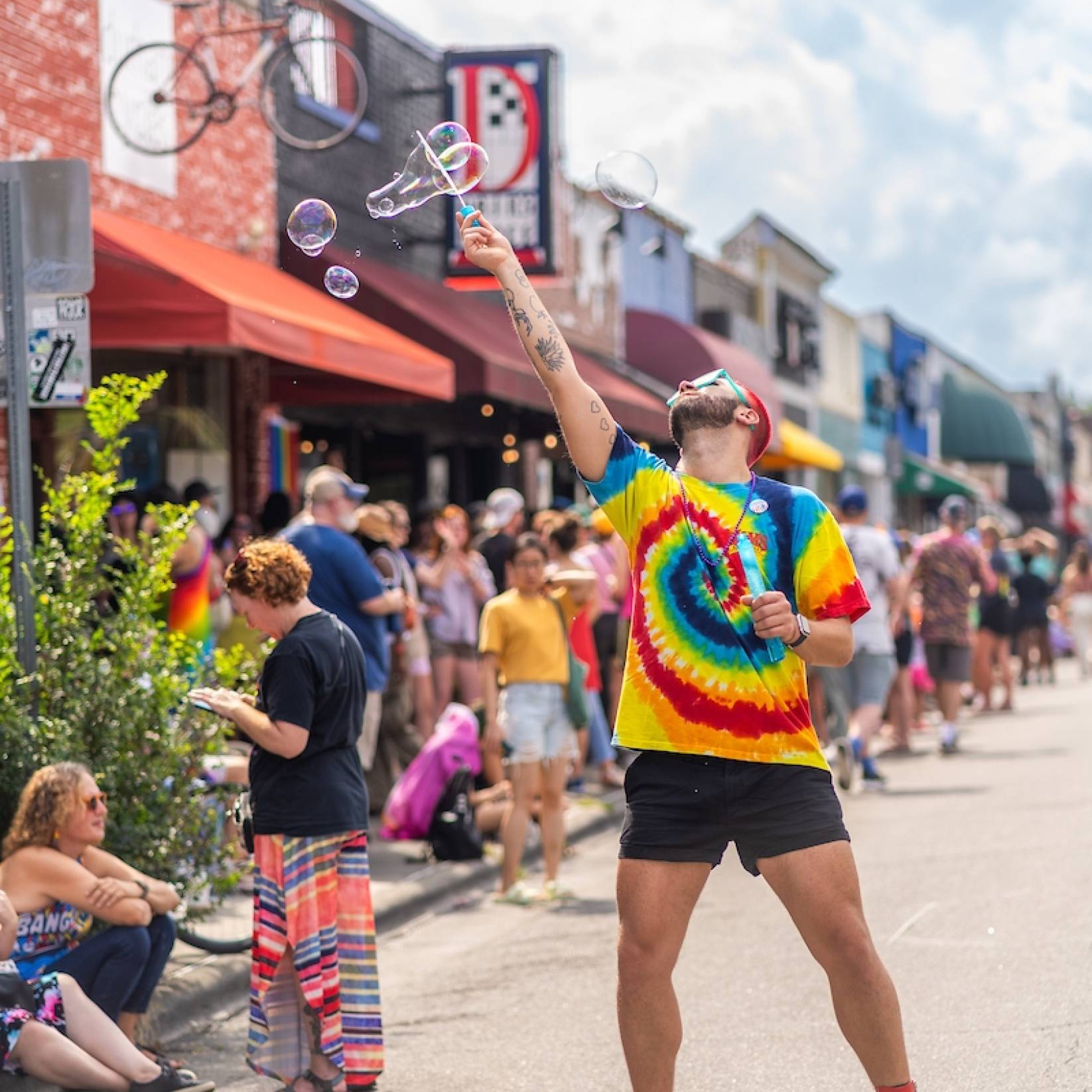 A man in a rainbow tie-dyed shirt blows bubbles in front of the crowd before The Pride: Durham, NC 2024 Pride Parade.