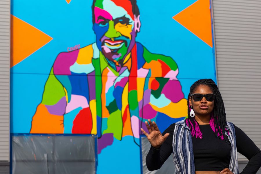 Artist Candy Carver stands in front of her mural of Phil Freelon at UHill.