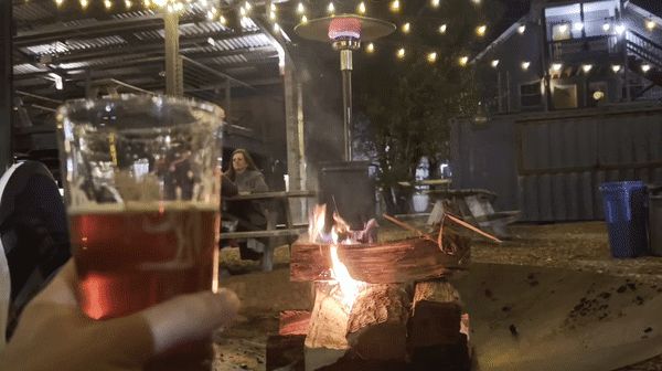 A person enjoys a beer while sitting by a fire pit at Durham's Ponysaurus.