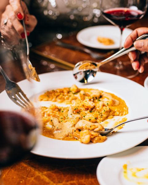 Hands dip utensils into a risotto shrimp dish at nana's In Durham.