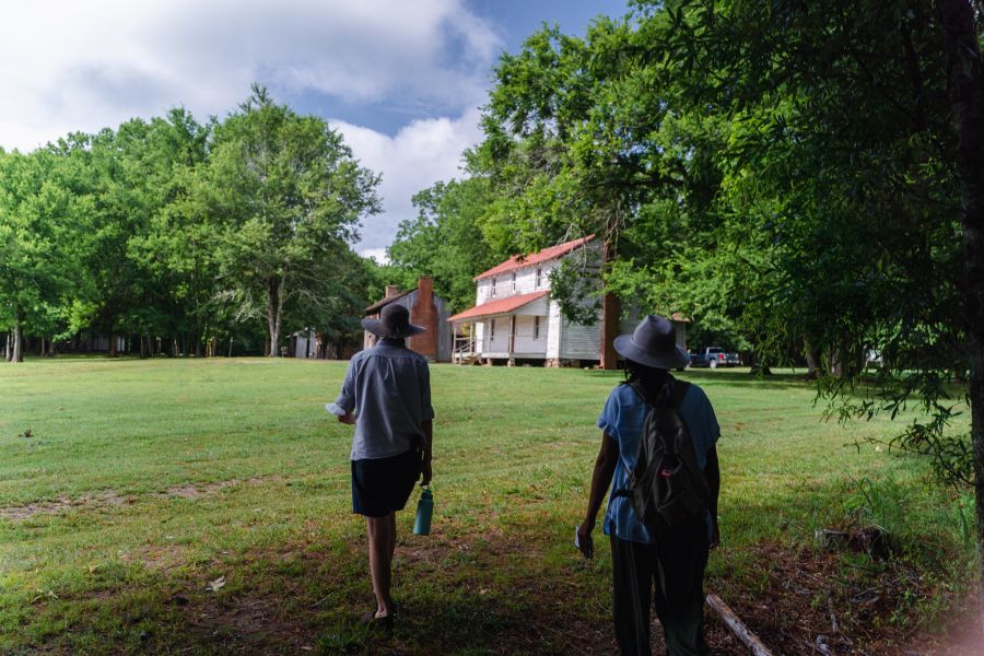 Two visitors walk through a field in front of one of the buildings at Historic Stagville.