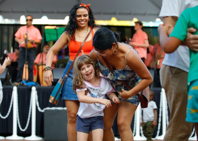 Two women dance with a little girl in front of a stage.