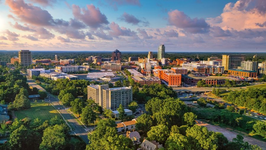 Green trees surround the Durham skyline under a pink and blue cloud strewn sky.