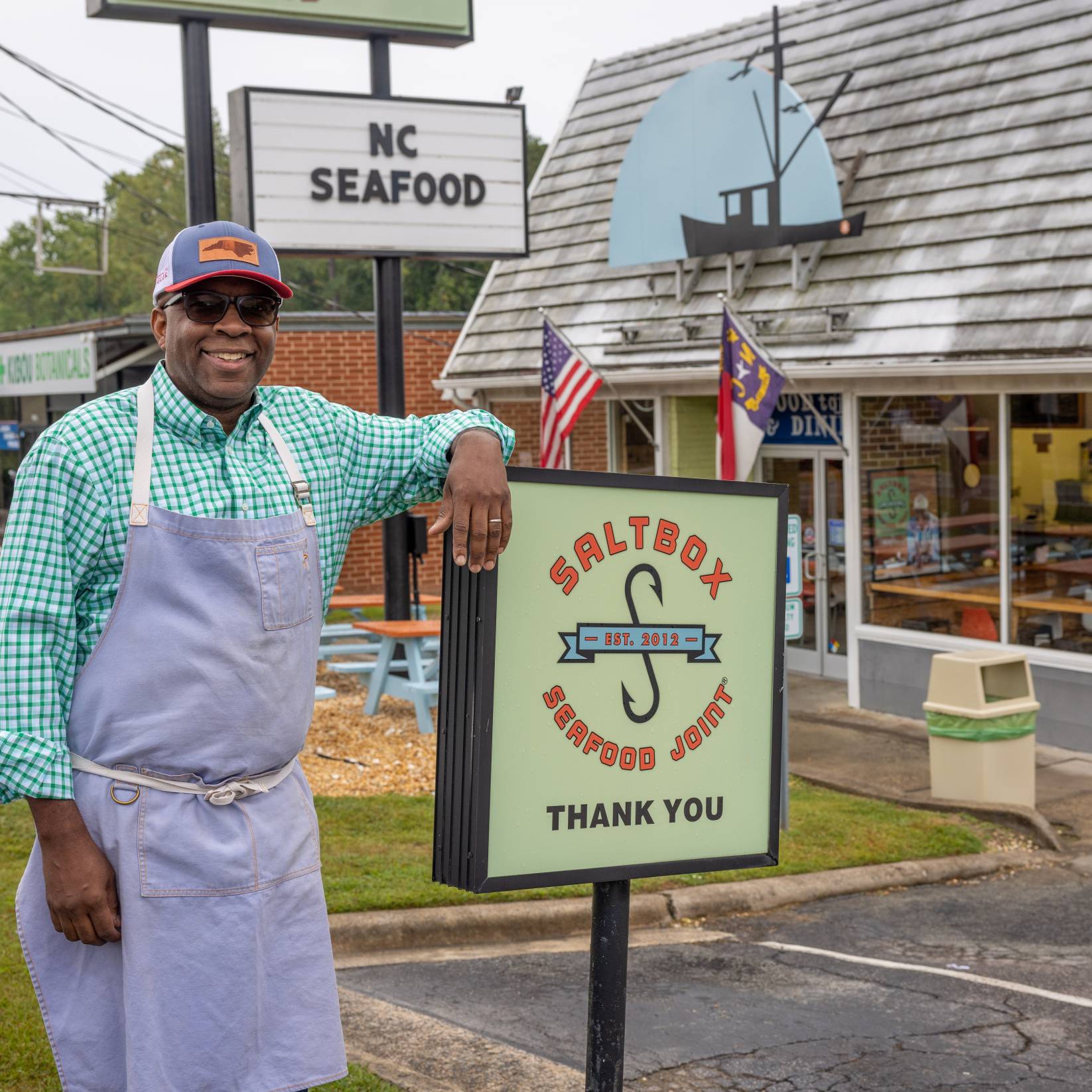 Chef Ricky Moore standing next to the sign at Saltbox Seafood Joint