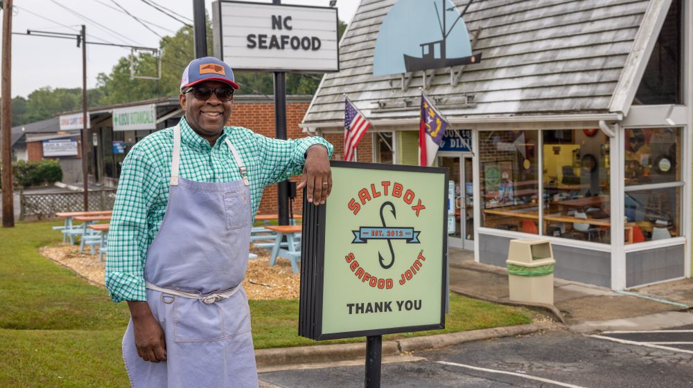 Chef Ricky Moore standing next to the sign at Saltbox Seafood Joint
