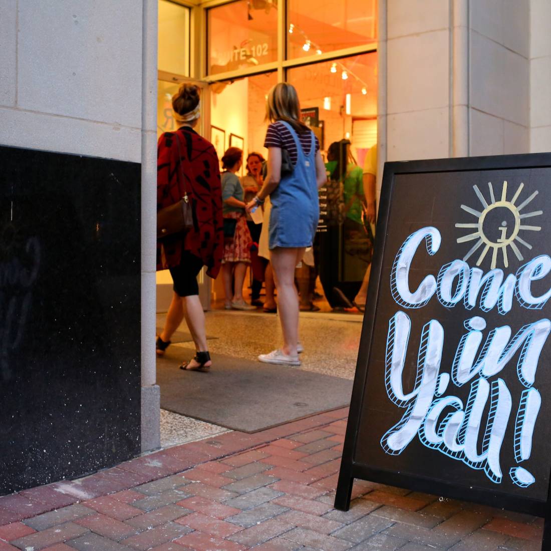 A black sandwich board in front of a building says "Come in y'all!"