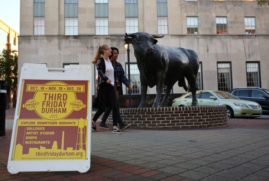 A couple walk between a Third Friday sign and Major the Bull in CCB Plaza.