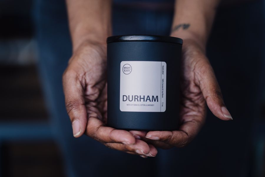 Hands hold one of Bright Black Candles' signature products, the Durham Candle.
