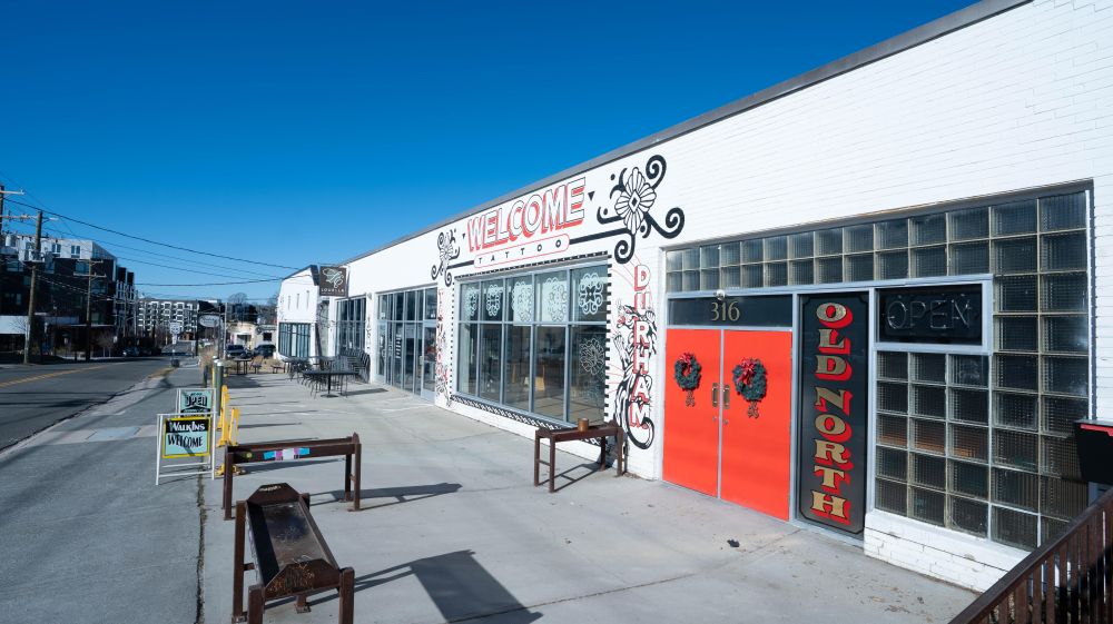 A blue sky runs over the storefronts of The Old North Bar and Welcome Tattoo.