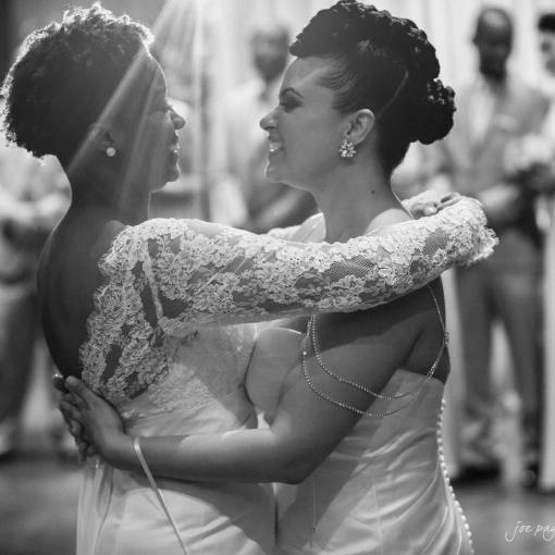 Brides embrace on the dance floor, smiling, as guests look on.