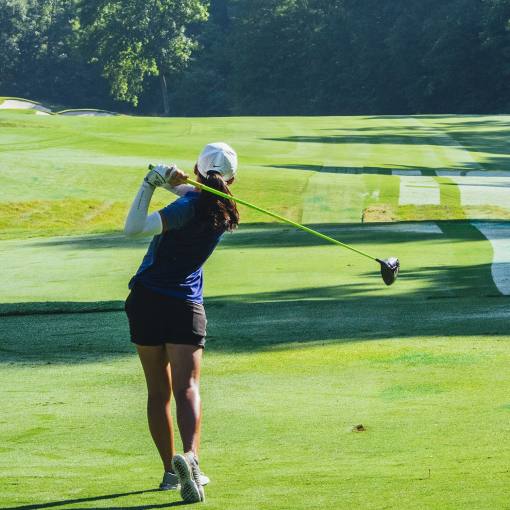 A golfer tees off on a serene course surrounded by trees.