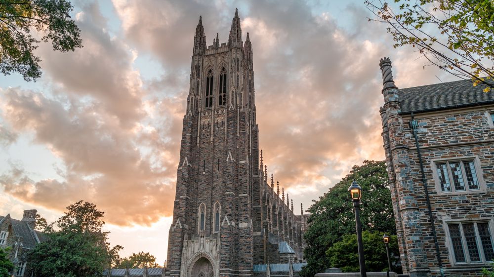 A cloud streaked sky shines pink behind the tower of Duke Chapel in Durham, NC.