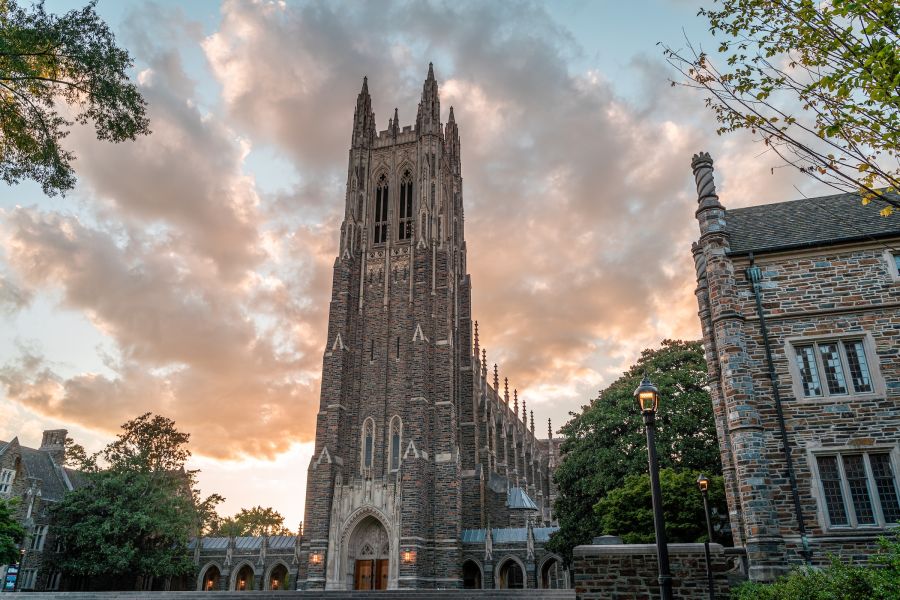 A cloud streaked sky shines pink behind the tower of Duke Chapel in Durham, NC.