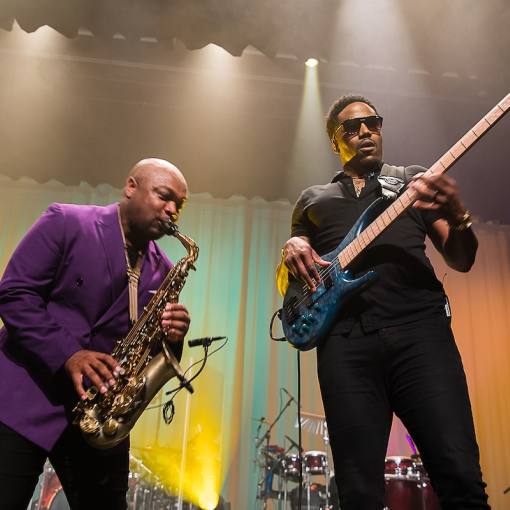 Two musicians performing on stage lit by yellow and green stage lights.