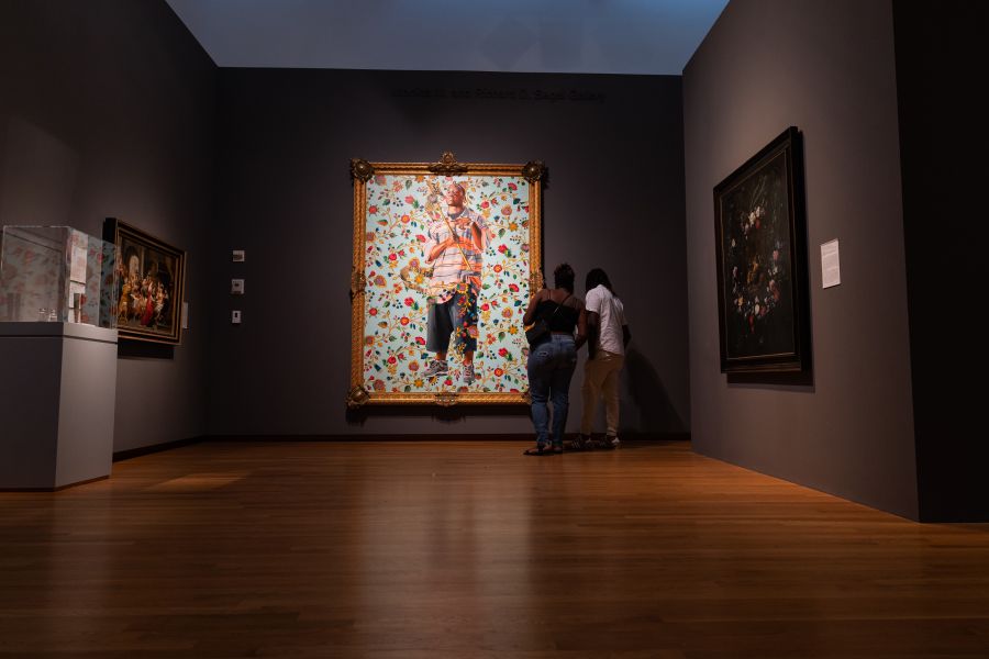 Visitors look at a painting in a dimly lit room at the Nasher Museum of Art