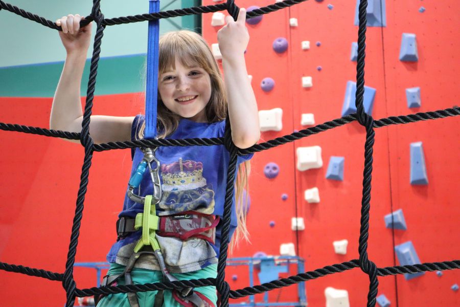 A young girl climbs the cargo rope wall at OC Aerial Indoor Adventure Park in Durham, NC